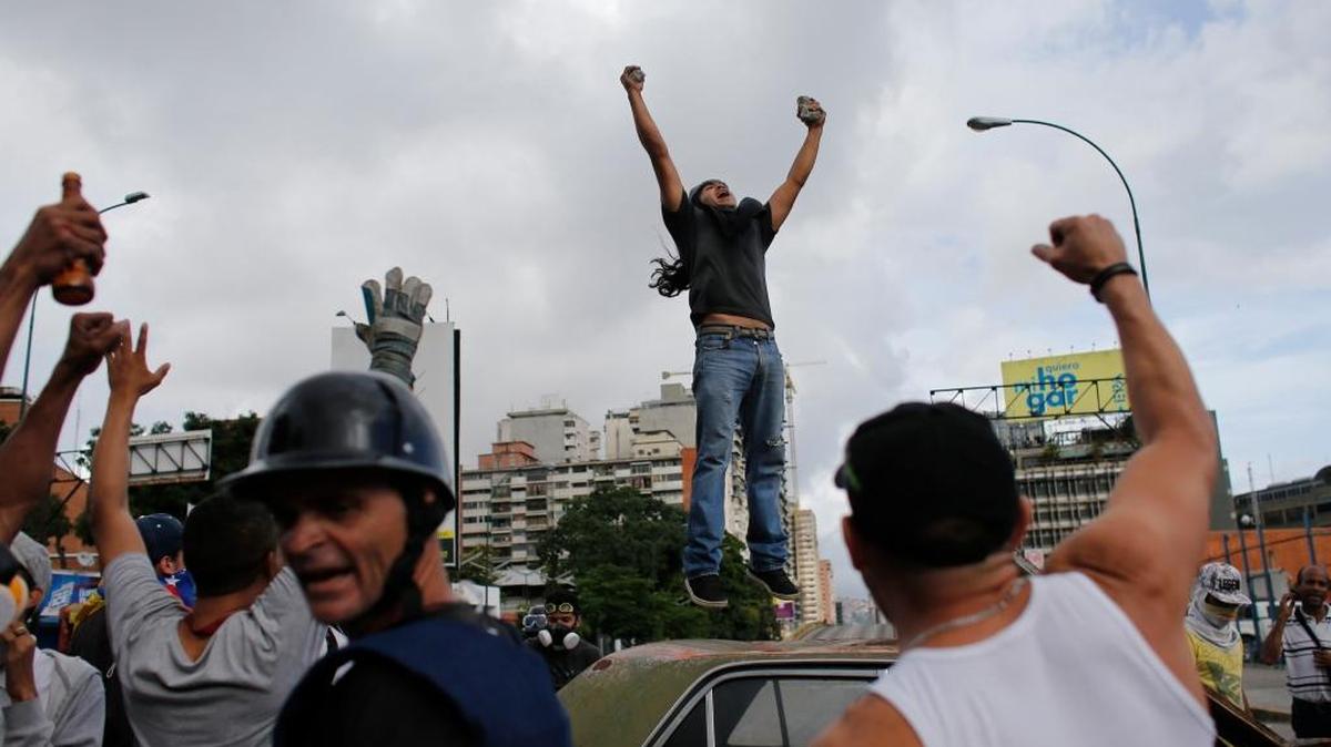 Un manifestante contra el gobierno de Maduro salta sobre un automóvil que luego fue incendiado, en protestas el 20 de julio en Caracas, Venezuela.