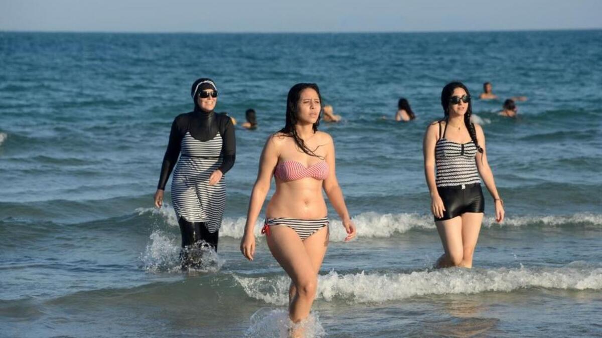 Varias tunecinas, una de ellas (izq.) vestida con un burkini, un traje de baño que cubre todo el cuerpo, creado para las mujeres musulmanas, salen del agua en una playa al noreste de la capital de Túnez.