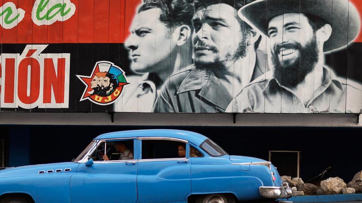 Un auto norteamericano viejo pasa en La Habana junto a un cartel con tres líderes revolucionarios: Julio Antonio Mella (izq.), Ernesto Che Guevara (centro) y Camilo Cienfuegos.