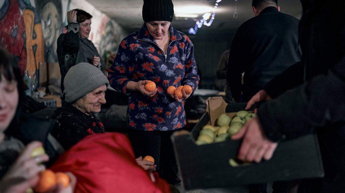 El capellán Leonid, un policía, obsequia a las personas mandarinas y manzanas antes de Navidad en el sótano de una casa de apartamentos utilizada como refugio antiaéreo en Avdiivka, región de Donetsk, Ucrania, el jueves 8 de diciembre de 2022. La gente ha estado viviendo en el sótano durante meses. escondiéndose de los bombardeos y ataques con cohetes rusos. (Foto AP/LIBKOS)
