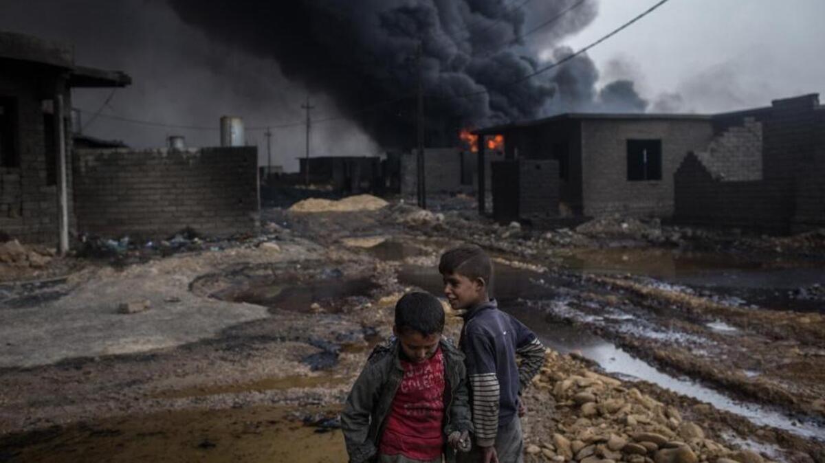 Dos niños juegan cerca de su casa y frente a un pozo de petróleo incendiado por miembros de ISIS, el 10 de noviembre, en Al Qayyarah, Irak.