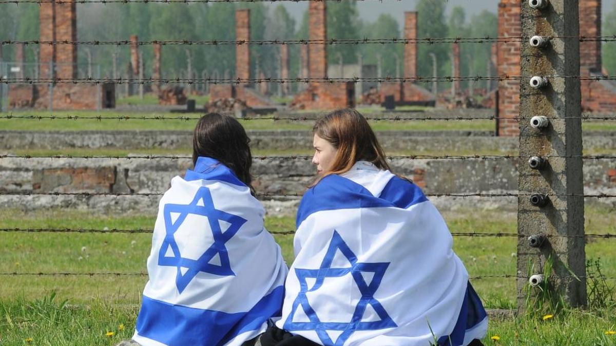 Dos jóvenes envueltas en la bandera israelí observan frente a las alambradas del campo de concentración de Auschwitz-Birkenau durante la Marcha de los Vivos, el 5 de mayo, en Brzezinka, Polonia, en la que se rinde homenaje a las víctimas del Holocausto.