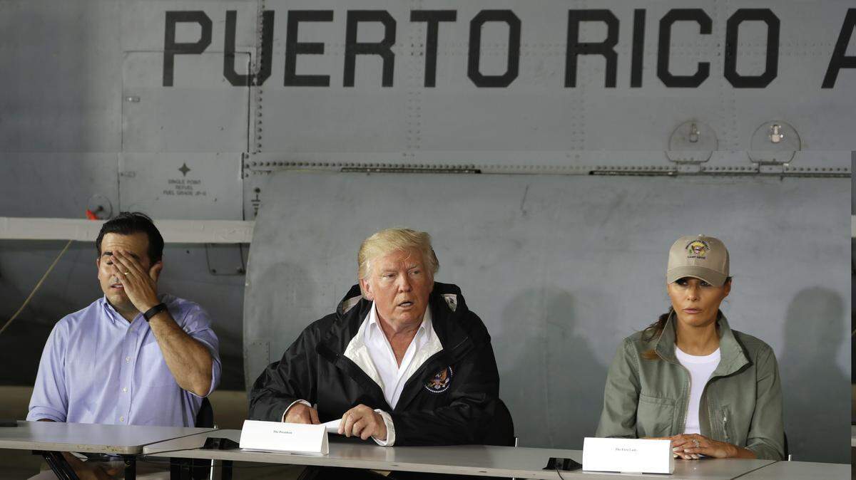 El presidente Donald Trump habla sobre los esfuerzos para ayudar a Puerto Rico tras el azote del huracán María, acompañado del gobernador Ricardo Roselló (izq.) y la primera dama Melania Trump, el 3 de octubre de 2017 en la Base Aérea Muñiz de la Guardia Nacional en San Juan.