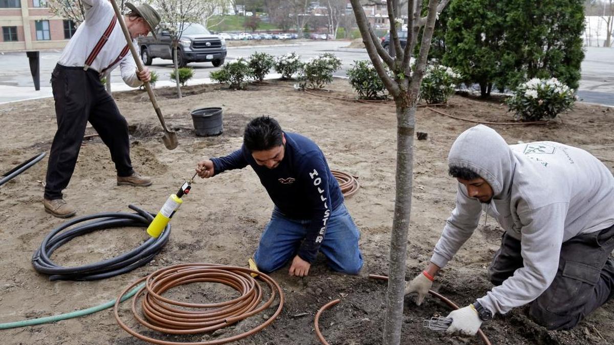 Stephen Faulkner (izq.), dueño de Faulkner's Landscaping & Nursery, instala un sistema de irrigación con los trabajadores Gonzalo García (centro) y Jalen Murchison, en un proyecto de jardinería en Manchester, New Hampshire. La dificultad para encontrar trabajadores temporales afecta a muchos negocios.
