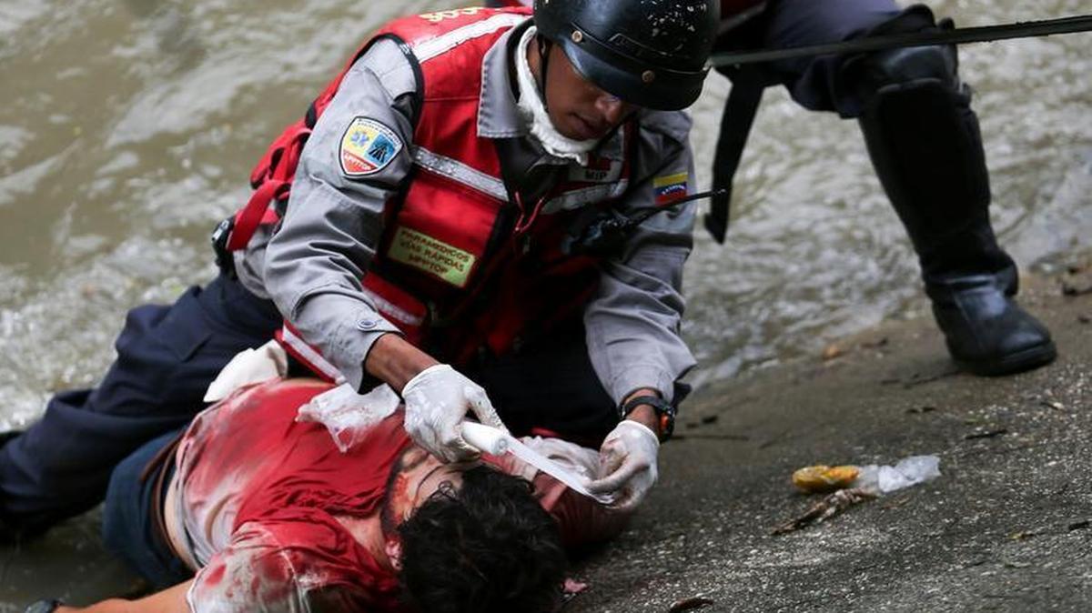 Rescatistas auxilian a un individuo que cayó al Río Guaire, el 19 de abril, tras ser impactado por una bomba lacrimógena lanzada por la Guardia Nacional Bolivariana durante una protesta en el sector de Petare (izquierda), un vecindario pobre de Caracas que aun permanece en protesta.