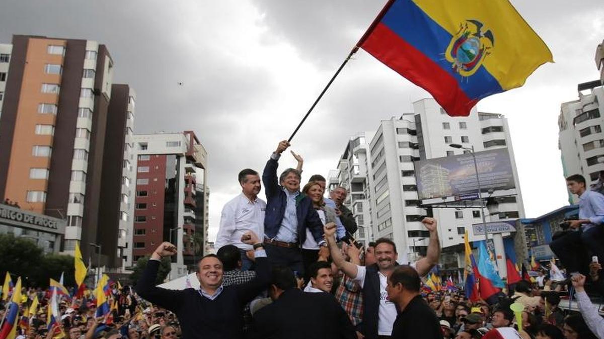 El candidato opositor Guillermo Lasso ondea una bandera ecuatoriana, acompañado por su esposa María de Lourdes Alcivar, su compañero de fórmula, Andrés Paez, y partidarios, el 21 de febrero, en Quito.