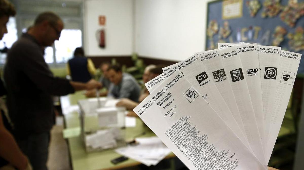 
Una persona muestra las papeletas de los diferentes partidos que concurren a las elecciones al Parlamento Catalán, el domingo 27, en Cataluña, mientras una persona deposita su voto en la urna.
