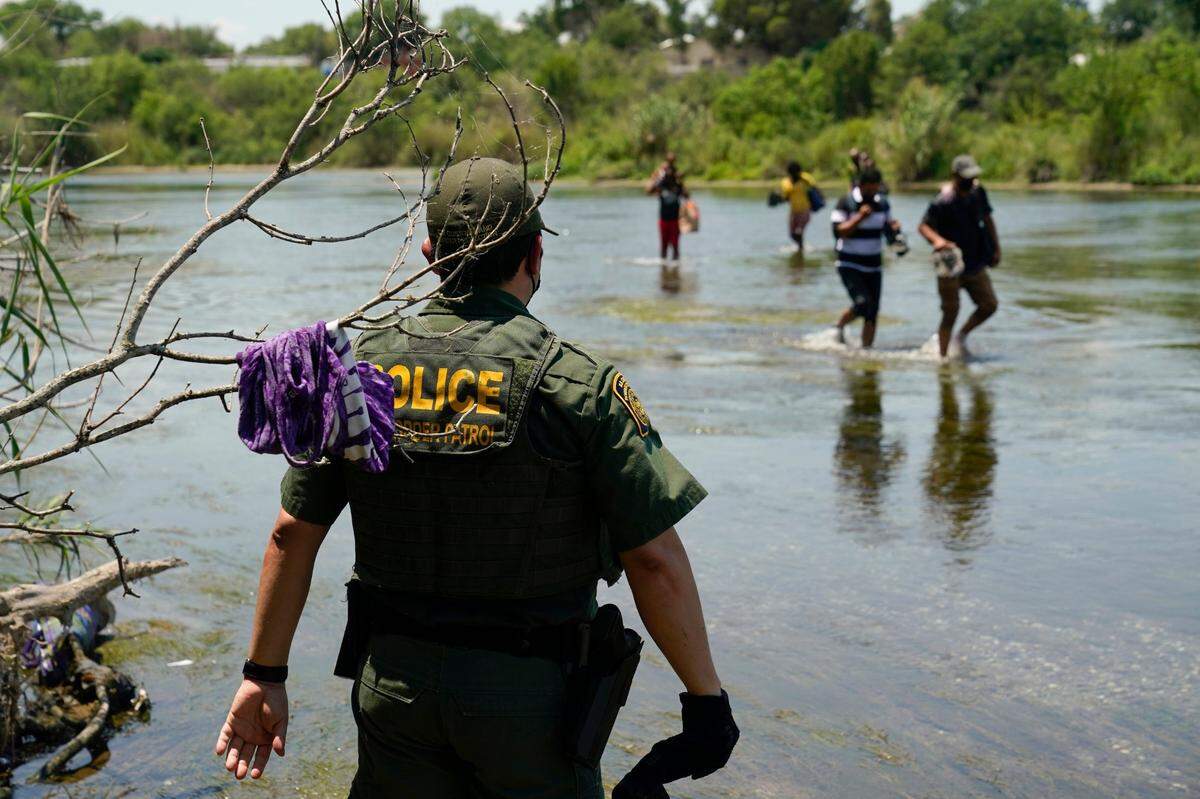 Un agente de la Patrulla Fronteriza de EEUU mira como un grupo de inmigrantes cruza el Río Grande, en camino a entregarse a las autoridades una vez que crucen la frontera México-Estados Unidos, cerca de Del Río, Texas.