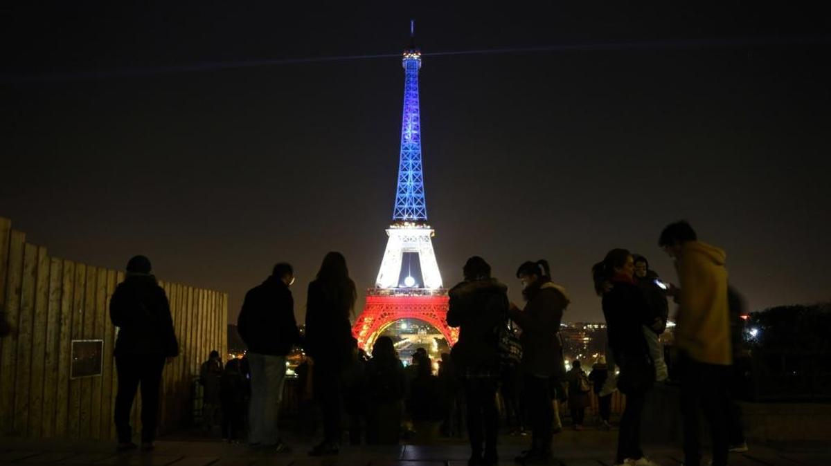 Algunas personas caminan en los alrededores de la Torre Eiffel iluminada con los colores de la bandera francesa, en honor a las víctimas de los ataques terroristas, en los que murieron 130 personas.