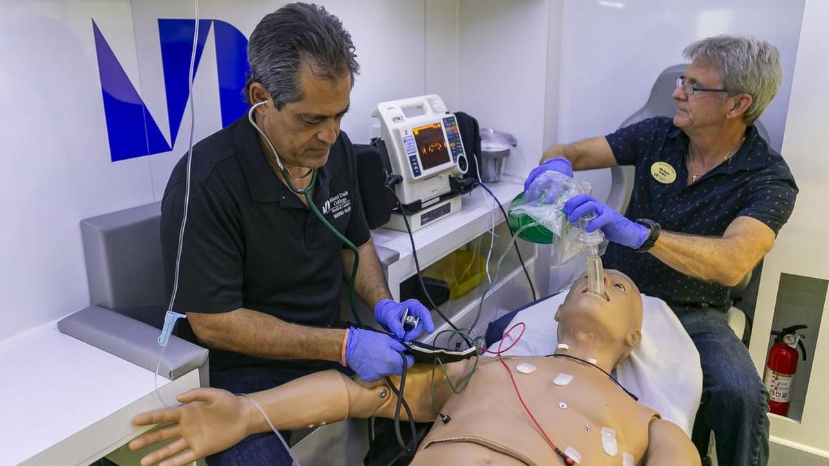 Los profesores Mario Alem (izq.)y Michael Yoder, realizan pruebas a un maniquí médico dentro de una simulación de ambulancia, el 15 de julio de 2019. Ambos trabajan en el nuevo Centro de Innovación, Aprendizaje y Simulación Médica del Campus Médico del MDC.
