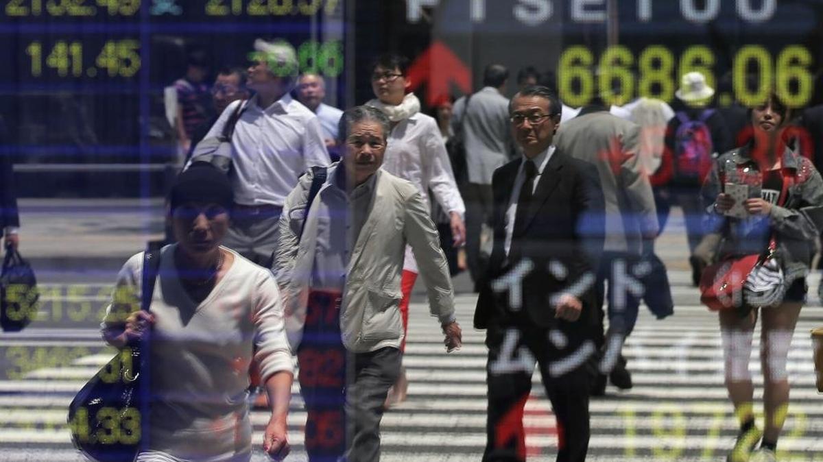 Un grupo de personas camina cerca de la pantalla de una firma bursátil en Tokio, Japón.