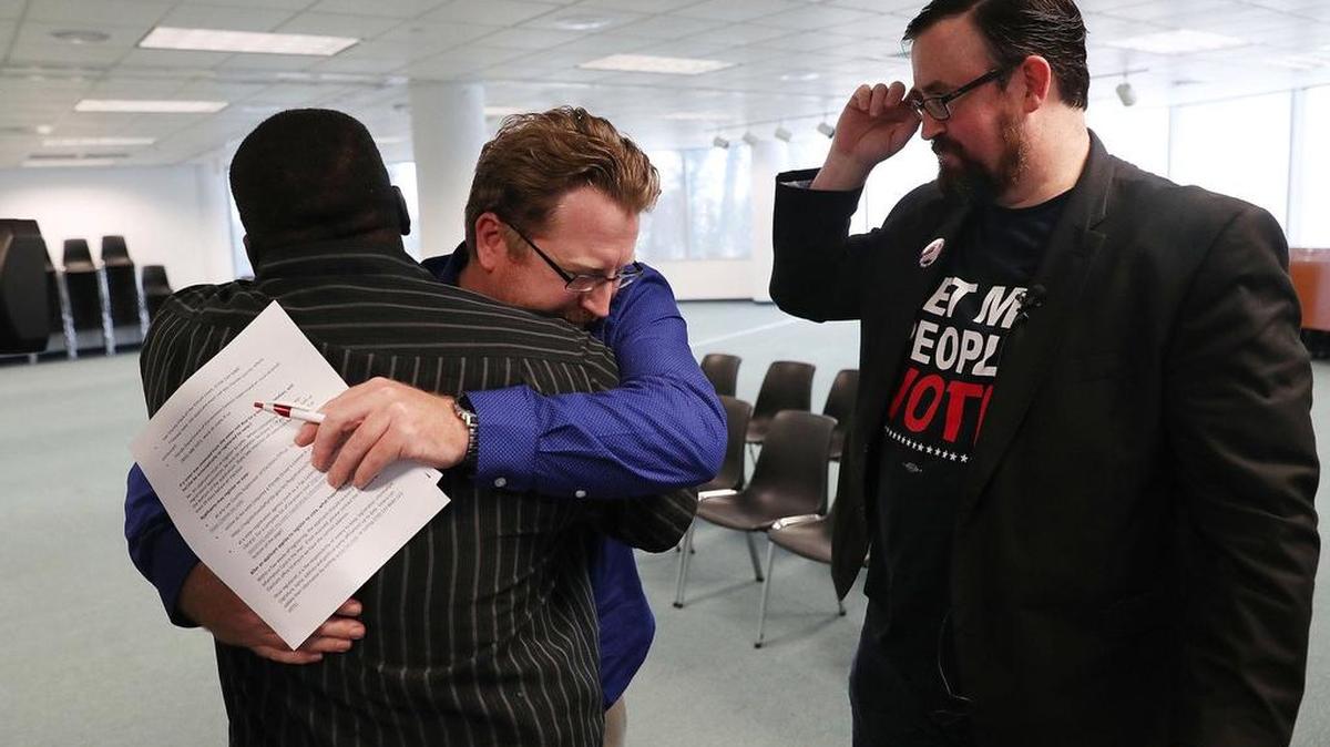 Lance Wissinger es abrazado por Permon Thomas (izq.), junto a Neil Volz (der.), mientras llenan la planilla de inscripción electoral, el 8 de enero en Fort Myers, Florida. Wissinger y Volz cumplieron sentencias por delitos graves, y gracias a la Enmienda 4 pudieron inscribirse para votar.