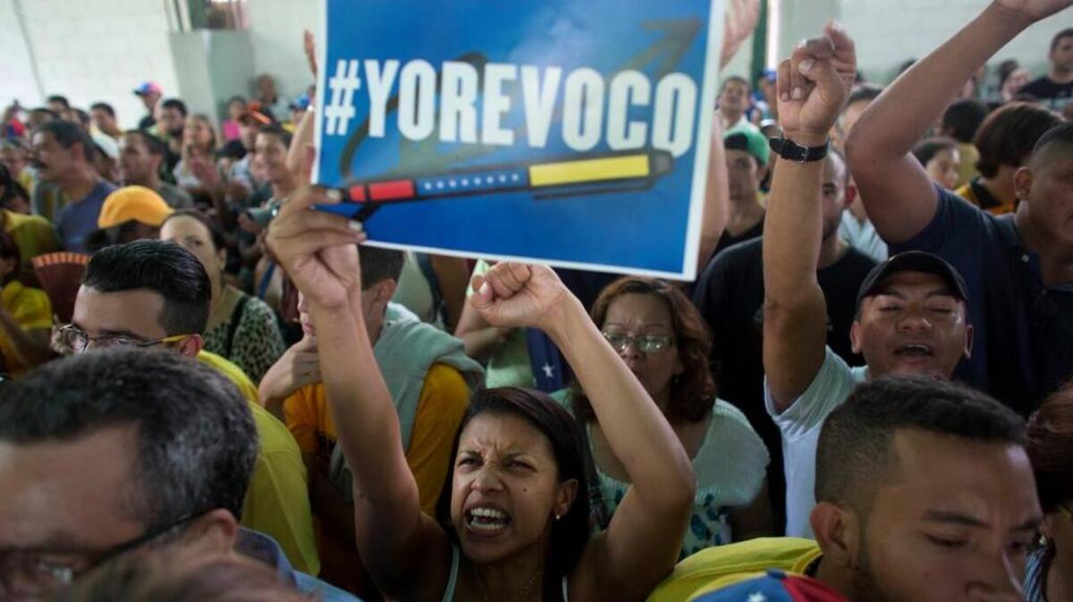 Una mujer sostiene un aviso que anuncia su deseo de revocar a Nicolás Maduro, cosa que el CNE hace cada día más difícil.