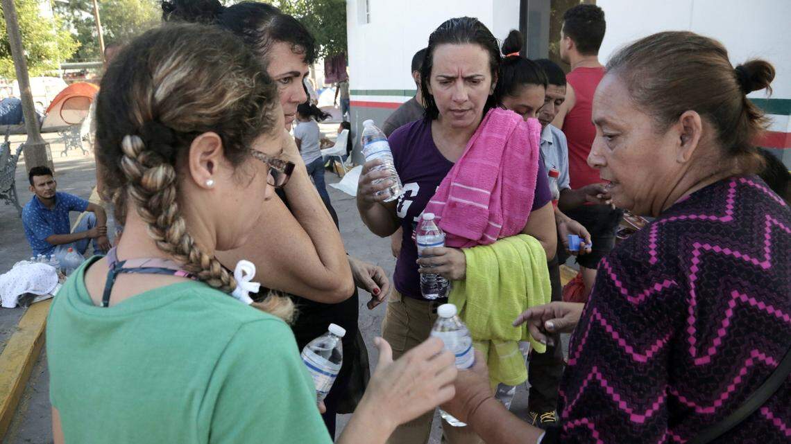 Una voluntaria mexicana, a la derecha, da agua a mujeres migrantes cubanas que viven en un campamento improvisado junto al Puente Internacional en Matamoros, México