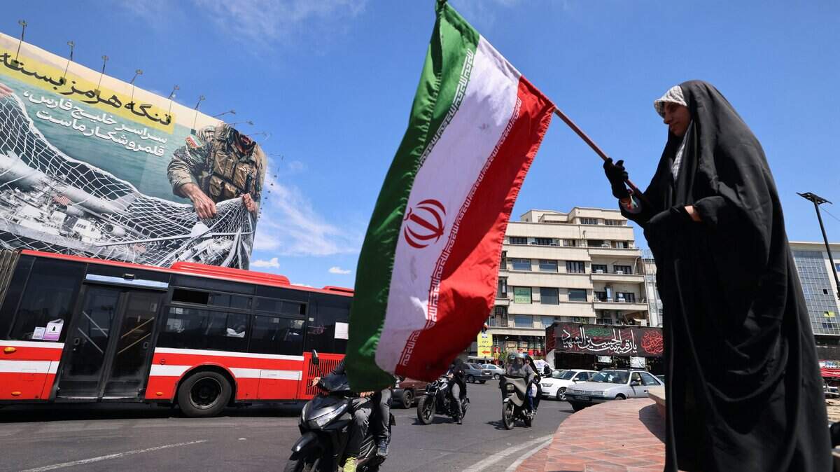 Una mujer ondea la bandera nacional de Irán frente a una enorme valla publicitaria que dice “El estrecho de Ormuz permanece cerrado” en la Plaza de la Revolución, en Teherán, el 12 de abril de 2026.