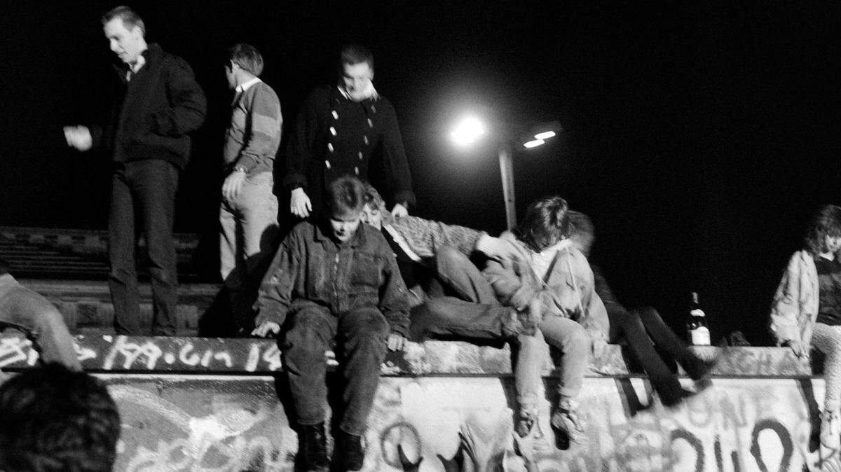 West-Berliner climb on the Berlin Wall on November 9, 1989 to ask for its fall. After months of mass protests against regime and amid a widening exodus of citizens to the West via Hungary, thousands of East Berliners on November 9, 1989 started streaming towards checkpoints leading to West Berlin, few hours after an East German official announced a decree stating that visas would be freely granted to those wanting to travel outside or leave the state and. / AFP PHOTO / Françoise CHAPTAL (Photo credit should read FRANCOISE CHAPTAL/AFP via Getty Images)