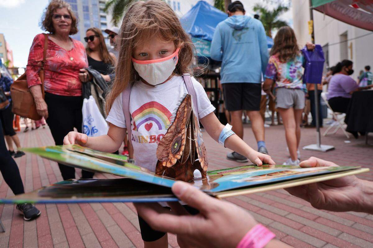 Shay Yuen looks at a pop-up book while her father, Brendon Yuen, 35, holds it at last year’s Miami Book Fair, which was a hybrid virtual and in-person event.