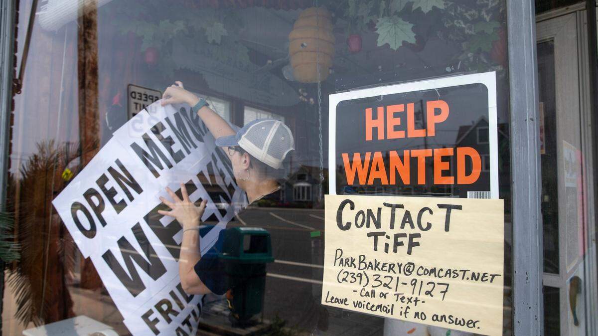 Foto de archivo del 23 de mayo de 2023 que muestra a Tiffany Hulse, administradora de la panadería Park Bakery, colocando un aviso de “abierto” al lado de uno solicitando ayuda, en Seaside Park, Nueva Jersey. El número de estadounidenses que solicitaron prestaciones por desempleo se redujo la semana que terminó el 3 de febrero de 2024. 