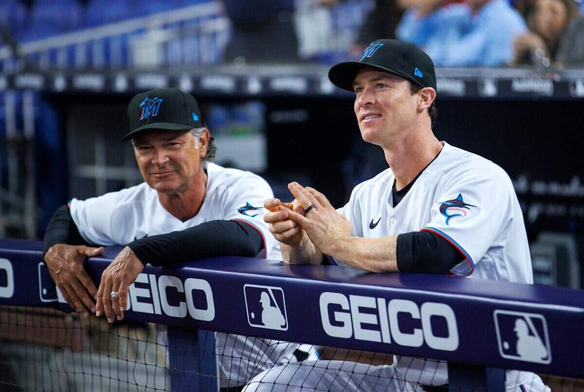 El manager de los Marlins Don Mattingly (izq.) y el tercera base Joey Wendle miran desde el dugout antes del inicio del partido contra los Filis de Filadelfia, el 14 de abril de 2022 en Miami.