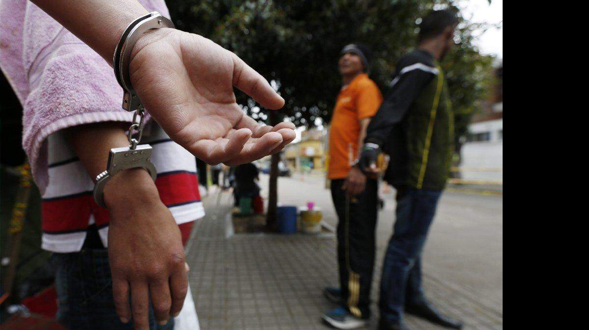 Los detenidos, esposados el uno al otro, de pie en un parque público en Bogotá, Colombia, el jueves, 11 de septiembre de 2014. Debido al hacinamiento en un centro de detención ubicado en la calle, el parque se ha convertido en zona de espera improvisada, donde los detenidos, más acusados de delitos menores, se mantienen durante días en espera de la decisión de un fiscal. Los prisioneros, que son detenidos por presuntos delitos que van desde el robo hasta el tráfico de drogas, son custodiados por grupos de seis agentes de la policía que se cambien después de ocho horas diarias.
