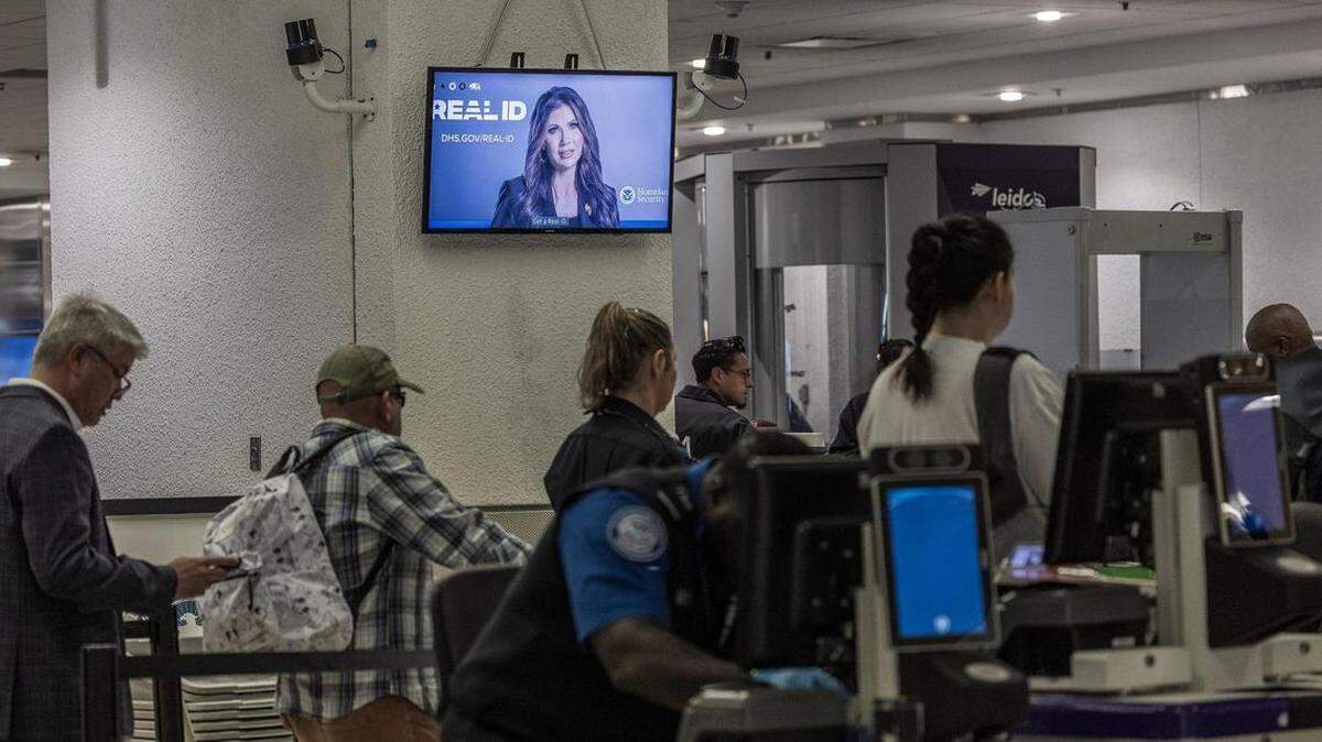 Pasajeros pasan por un puesto de control mientras se reproduce información sobre la REAL ID en una pantalla en el Aeropuerto Internacional de Miami, el miércoles 7 de mayo de 2025.