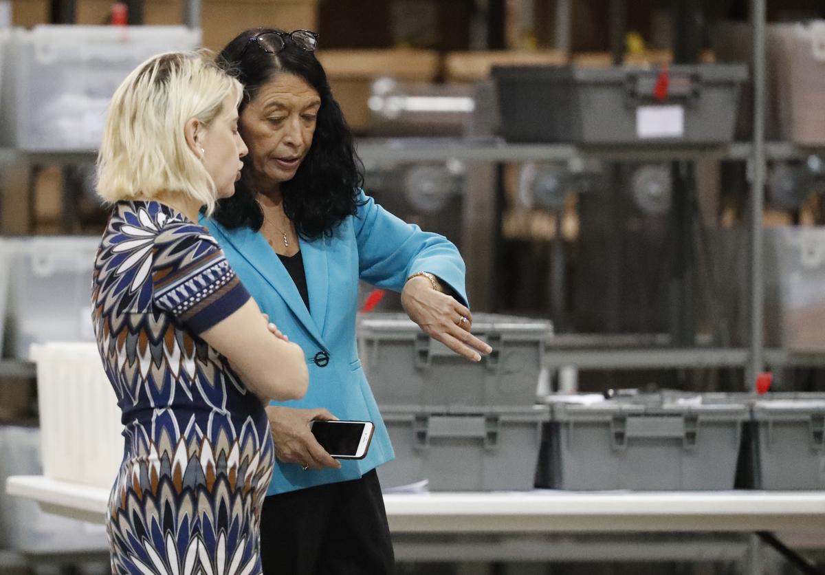 Susan Bucher (con la chaqueta azul), supervisora de Elecciones de Palm Beach, mira la hora mientras habla con una empleada durante el recuento, el 15 de noviembre del 2018 en West Palm Beach, Florida.