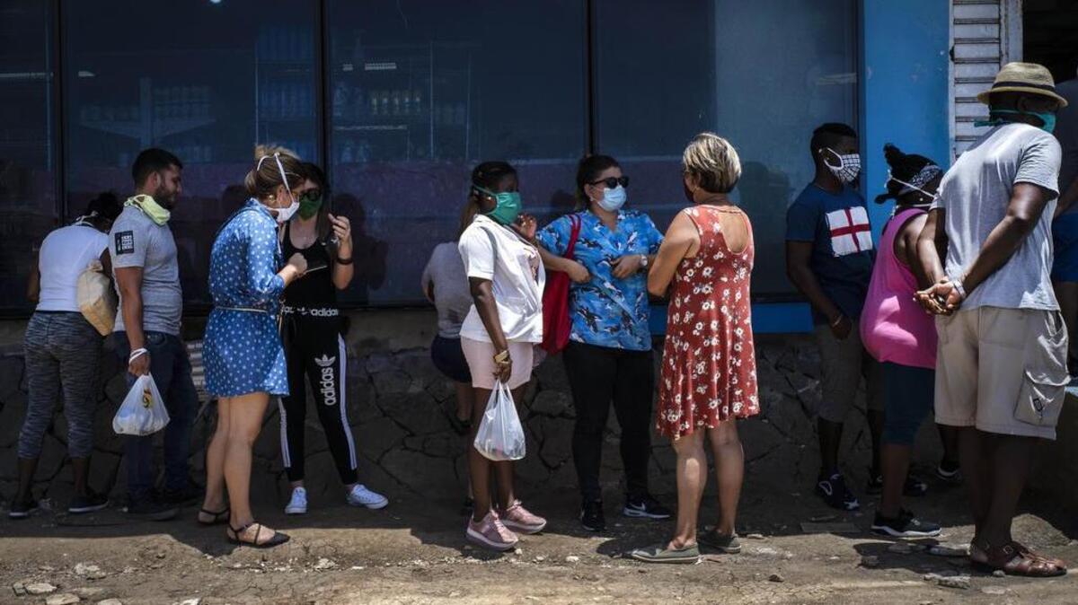 Afuera de una tienda estatal de comida, personas con mascarillas para protegerse del nuevo coronavirus esperan en fila para entrar en La Habana, Cuba, el martes 19 de mayo de 2020.