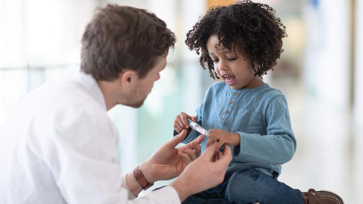 Un niño de 4 o 5 años mira con intriga el bolígrafo para la diabetes que le muestra el médico.