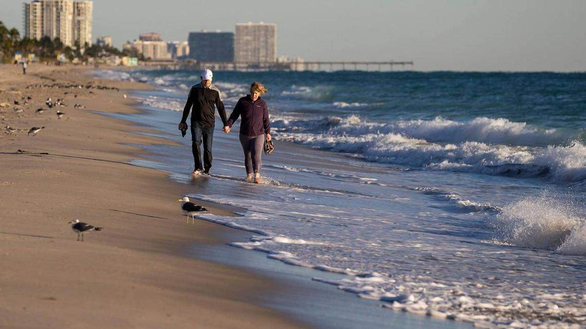 Jason Rayburn y Natalie Suiter caminan por la orilla con temperaturas en torno a los 40 grados el sábado, 14 de enero de 2023, en Hollywood, Florida.