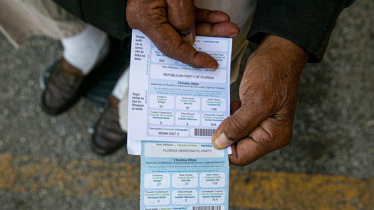 Juan Salazar, de 77 años, sostiene sus tarjetas de registro de votante frente a su apartamento en el vecindario de La Pequeña Habana en Miami. Salazar explicó que su afiliación partidaria cambió de demócrata a republicana sin su permiso. 