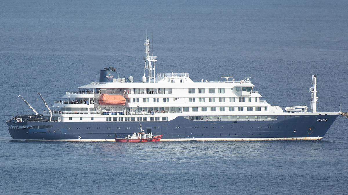 Una lancha ambulancia que transporta a miembros de la tripulación con trajes de protección biológica se acerca a la puerta de práctico en el lado de estribor del crucero MV Hondius, mientras permanece detenido frente al puerto de Praia, la capital de Cabo Verde, el 5 de mayo de 2026, mientras los pasajeros observan desde las cubiertas.