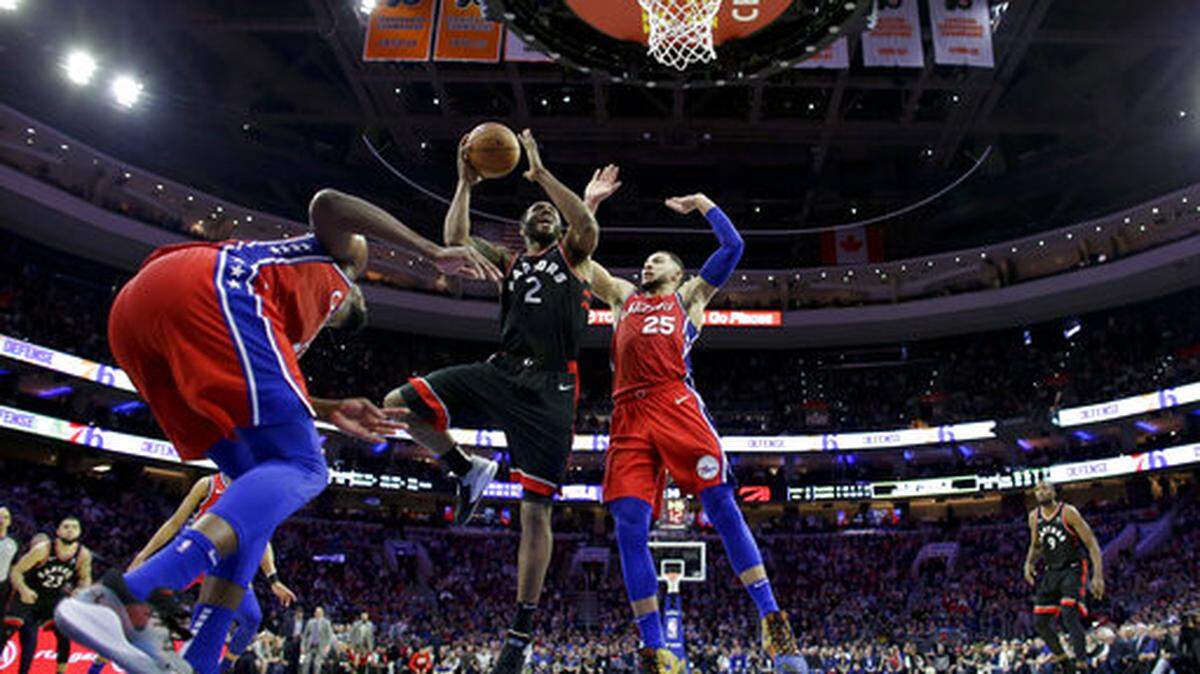 Los jugadores de los 76ers Ben Simmons (der.) y Joel Embiid (izq.) tratan de impedir la canasta del delantero de los Raptors Kawhi Leonard este 5 de febrero en Filadelfia.
