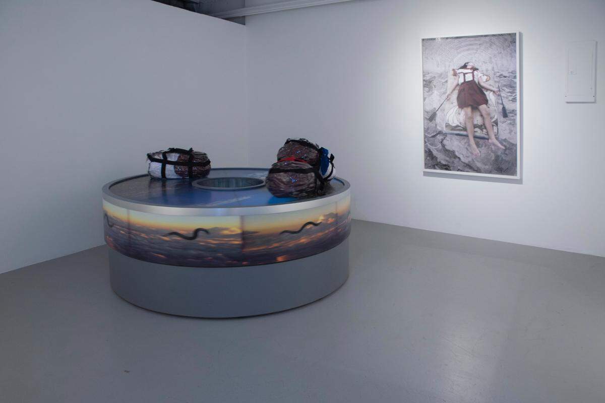 ‘Perpetual Movement of the Cuban Worm Between Two Shores (uniforms)’, 2018-2023, de Sandra Ramos. Caja de luz. Instalación cinética (Un carrusel de equipaje y uniformes escolares de primaria típicos de las escuelas cubanas, empacados en maletines transparentes). 81 pulgadas de diámetro