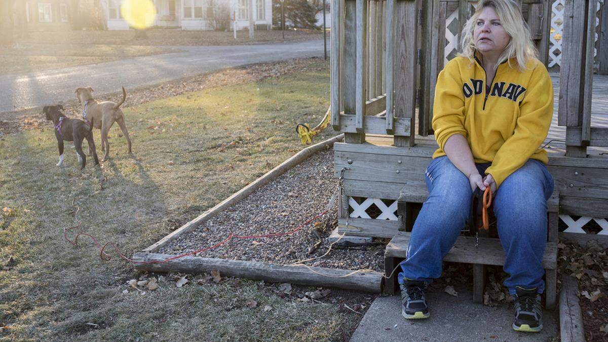 Danette Lake en la entrada de su casa después de pasear a sus perros, Zoe y Chloe. Un doctor le dijo que la cirugía de reemplazo de rodilla podía reducir su dolor en un 75 por ciento. Un año después del procedimiento, todavía siente dolor y no puede trabajar.
