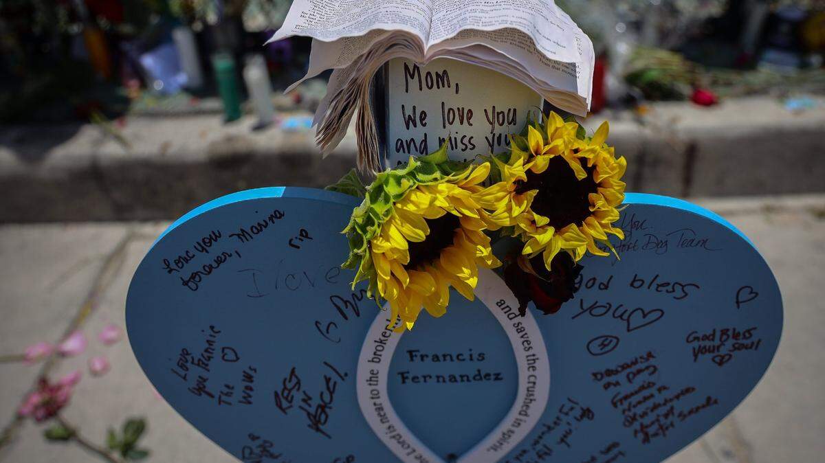 Corazones de madera con los nombres de las víctimas junto a las foto y flores el 11 de julio de 2021 cerca del lugar del memorial a las víctimas del derrumbe en Surfside, Florida.