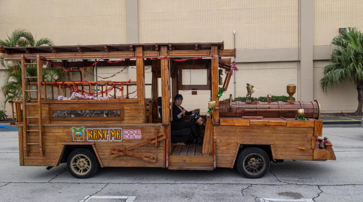 Xiomara Yani Pérez, propietaria del vehículo de madera junto con su esposo, posa junto al tren de madera, un vagón convertido para que parezca un tren, en el estacionamiento del Westland Mall en Hialeah. El vehículo se alquila para eventos, políticos o cualquier persona que busque un viaje único. Hialeah, Florida, 22 de diciembre de 2023 -
