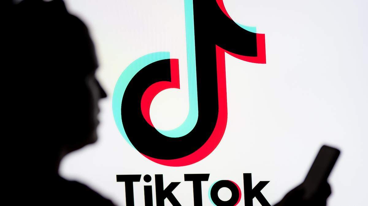 En esta ilustración fotográfica, se ve a una mujer mirando un teléfono inteligente con el logotipo de TikTok mostrado en el fondo.