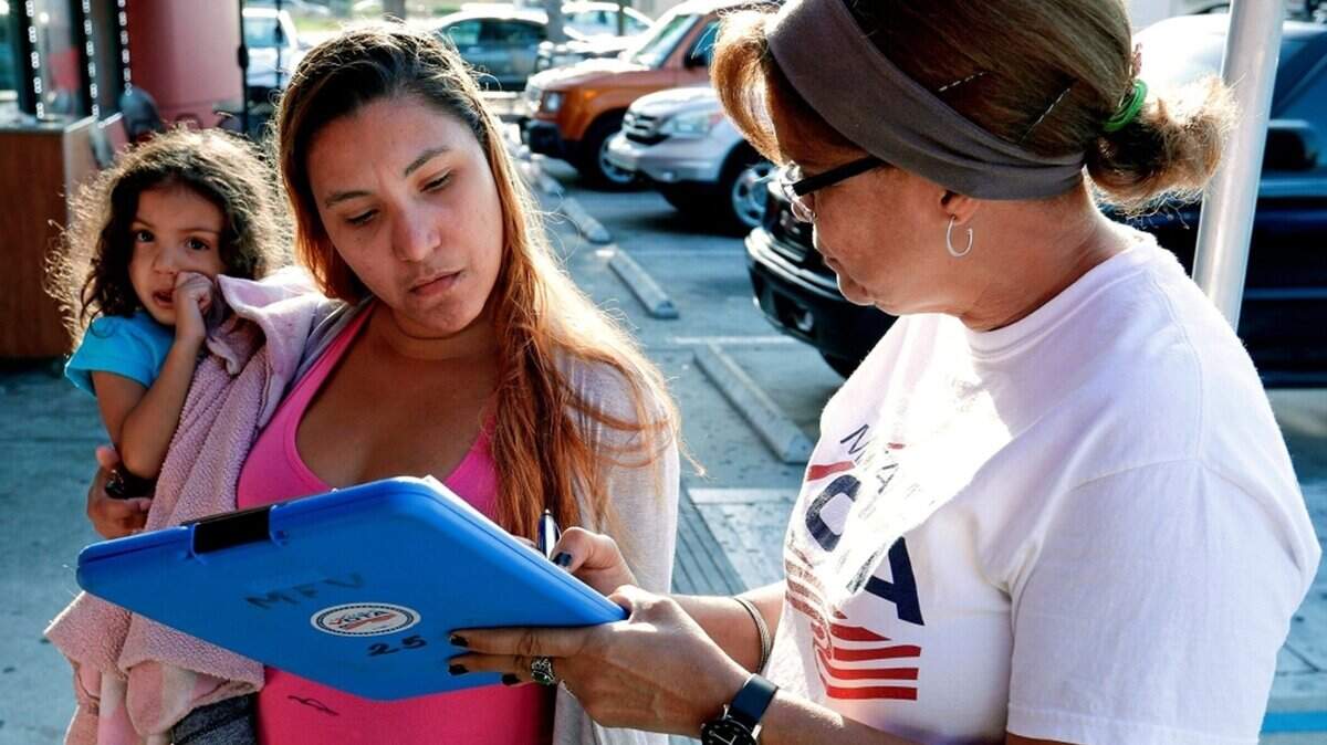 In this April 12, 2018 photo, Michelle Ortiz, who was born in New York to Puerto Rican parents and recently moved to Florida, holds her daughter as she registers to vote with the help of volunteer Carmina Redonet, right, in Orlando, Florida. Political operatives, pollsters and politicians in at least four states are working hard right now to find Puerto Ricans who are eligible to vote and whose party affiliation may be up for grabs. (AP Photo/John Raoux)