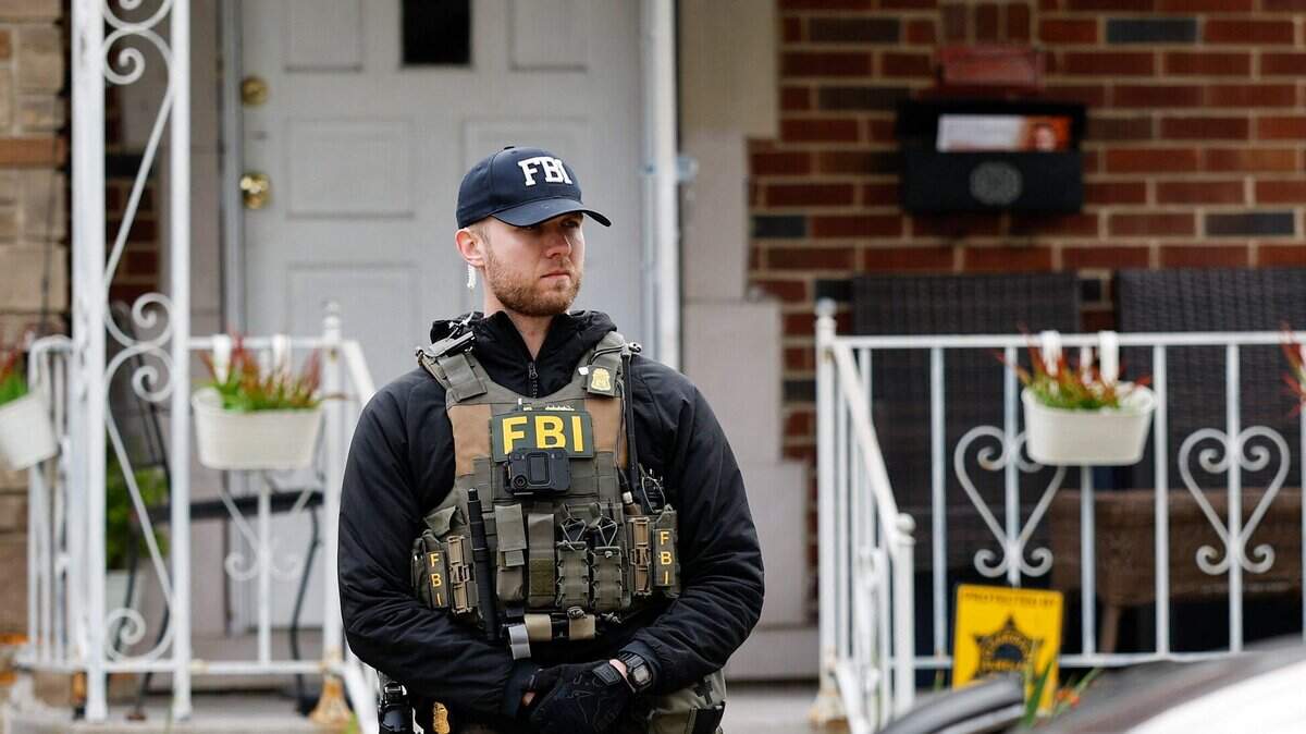 A member of the FBI Joint Terrorism Task Force stands watch in the front yard as law enforcement searches a home in Dearborn, Michigan, on October 31, 2025. FBI Director Kash Patel said Friday that the agency had thwarted a "potential terrorist attack" planned in the northern state of Michigan over Halloween weekend. Patel said the FBI arrested multiple subjects. (Photo by JEFF KOWALSKY / AFP) (Photo by JEFF KOWALSKY/AFP via Getty Images)