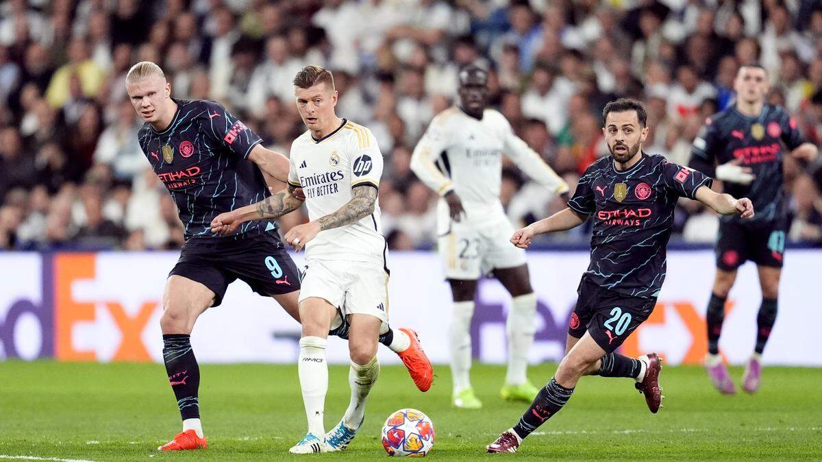 Los jugadores del Manchester City Erling Haaland (izq.) y Bernardo Silva (der.) luchan por la pelota con Toni Kroos, del Real Madrid, en el partido de ida de los cuartos de final de la Liga de Campeones, celebrado el 9 de abril de 2024 en el estadio Santiago Bernabéu de la capital española.
