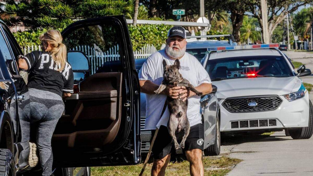 Un hombre con su perro cargado se acerca a su auto el sábado 27 de enero de 2024, después que la policía de Miami-Dade allanó a una casa por usarse como clínica veterinaria sin licencia.
