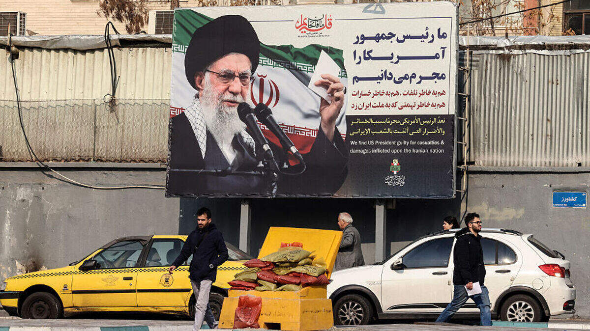 Unos iraníes pasan junto a una valla publicitaria que muestra al líder supremo iraní, el ayatolá Ali Khamenei, con mensajes antiestadounidenses, en Teherán, el 27 de enero de 2026.