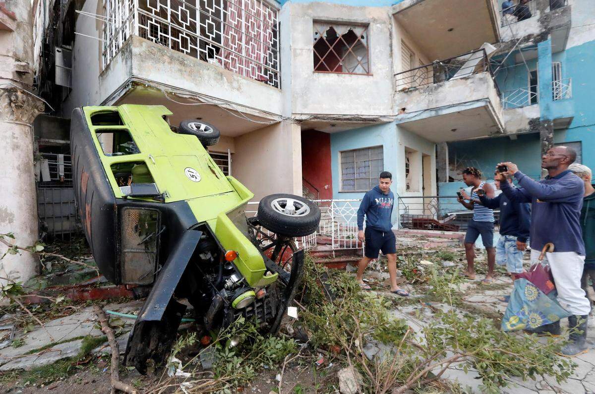 Varias personas toman fotografías de un vehículo averiado tras el paso de un tornado, este lunes, en La Habana.
