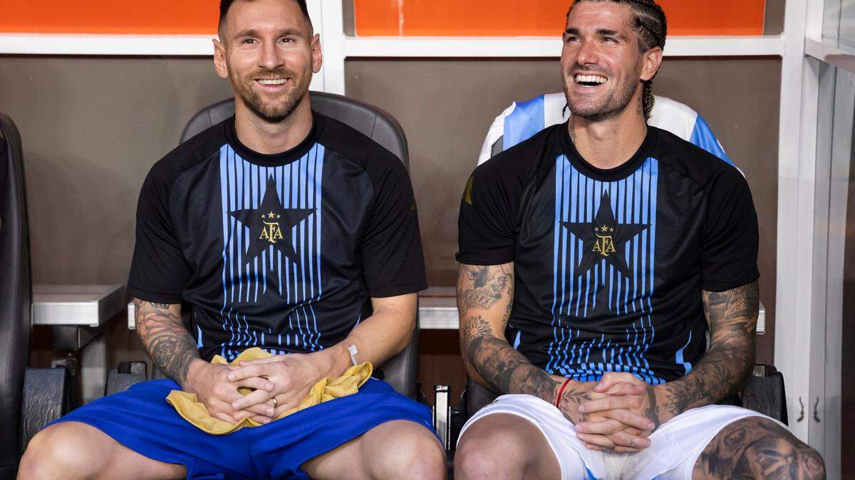 Argentina forward Lionel Messi (10) and midfielder Rodrigo De Paul (7) look on from the bench before the start of his CONMEBOL Copa America 2024 group A soccer match against Peru at Hard Rock Stadium on Saturday, June 29, 2024, in Miami Gardens, Fla.