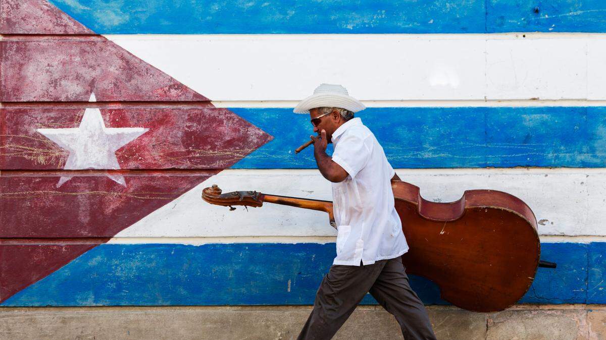La Academia Cubana de la Lengua concluye un proyecto para incorporar 100 cubanismos en la próxima edición del Diccionario de la Lengua Española (DLE) en 2026. En esta foto de archivo, un músico camina con su contrabajo frente a un mural de la bandera de Cuba.
