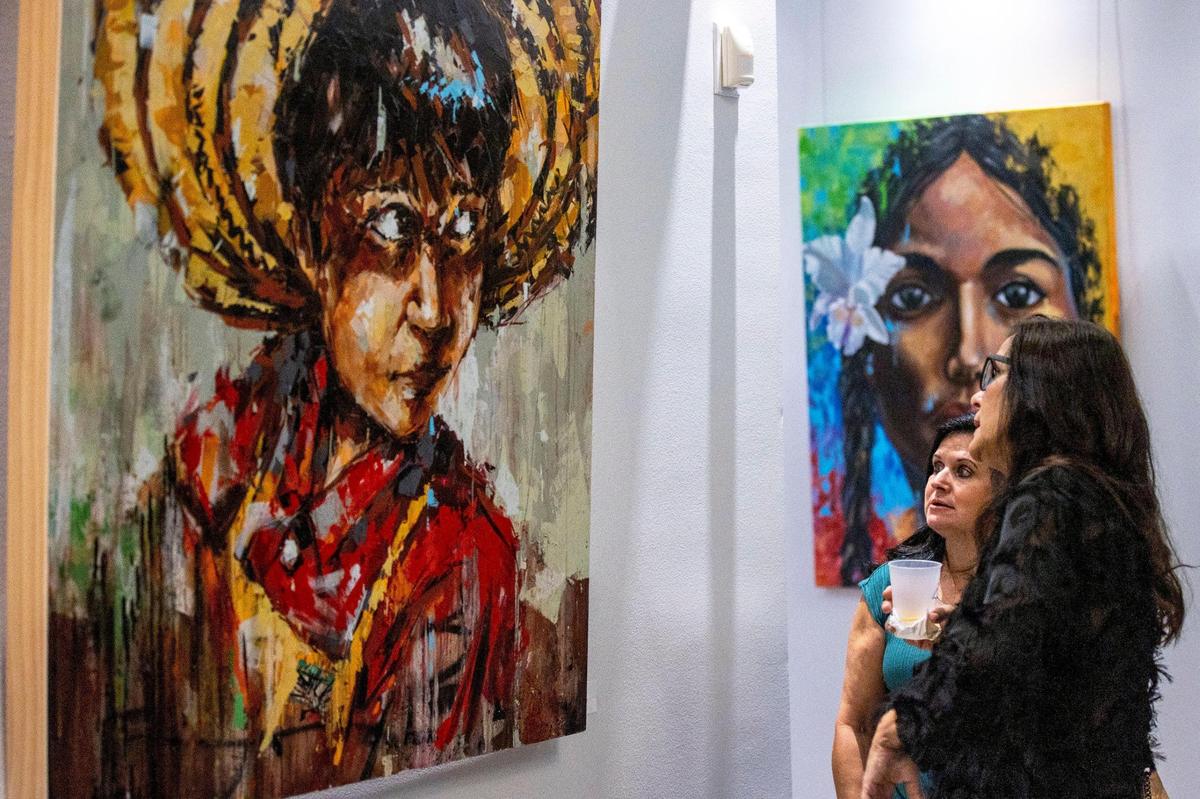 Las personas miran las obras de arte durante la exposición de artistas latinoamericanos en el Milander Center en Hialeah. En segundo plano, la obra “Chapolera”, que representa a las mujeres cafetaleras de Colombia, de Oscar Esteban Martínez, el viernes 30 de septiembre de 2022.
