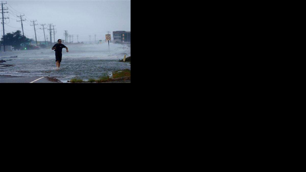 En esta foto del 4 de julio del 2014 se ve a un hombre cruzando la inundada carretera 64 durante el paso del huracán Arthur por Nags Head, Carolina del Norte.