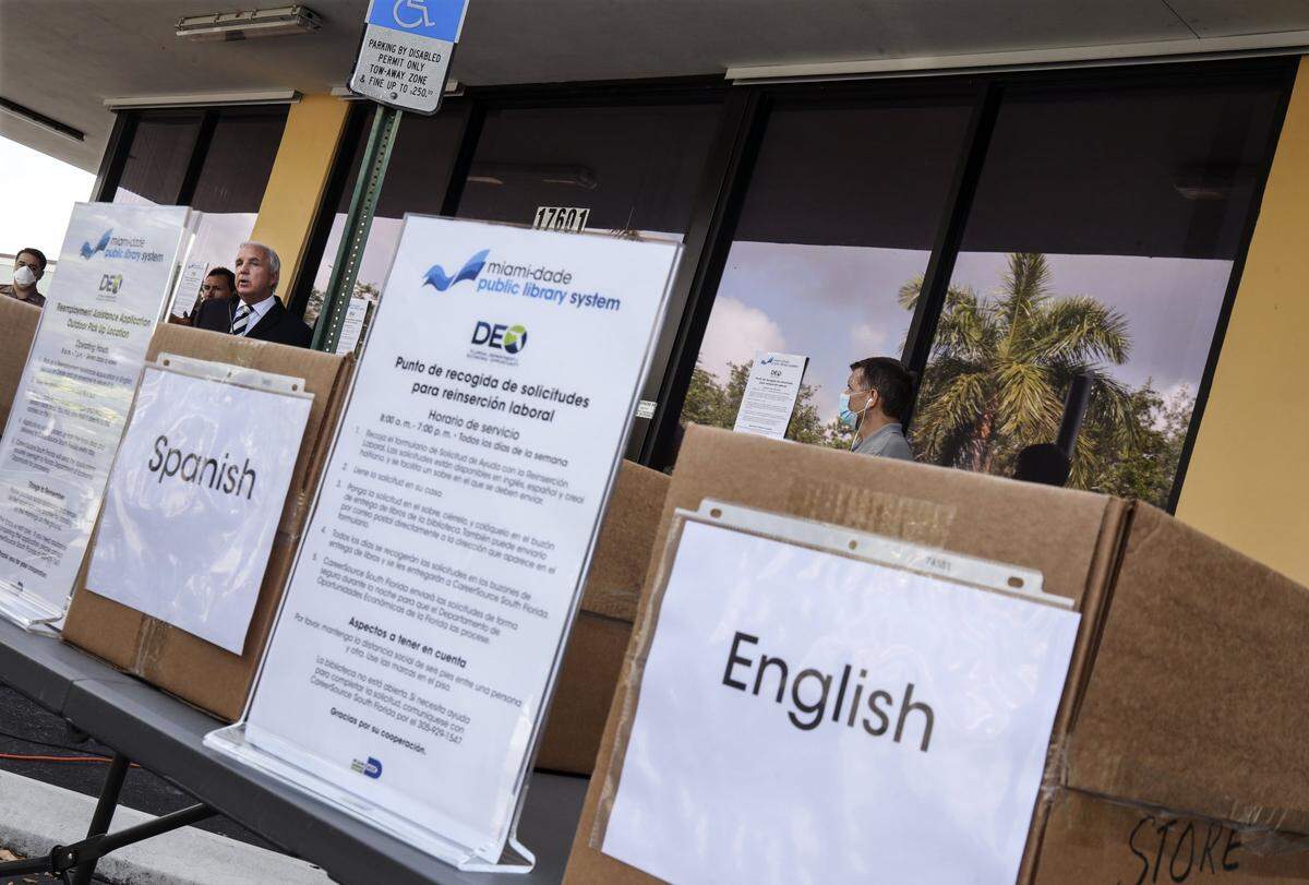 Boxes containing applications in multiple languages are displayed outside as Miami-Dade Mayor Carlos Gimenez, left, announced the opening of 26 Miami-Dade Public Library branches to pick up and drop off paper copies of unemployment benefit applications during a press conference at Palm Springs North Branch Library in Hialeah, Florida, on Wednesday, April 8, 2020.
