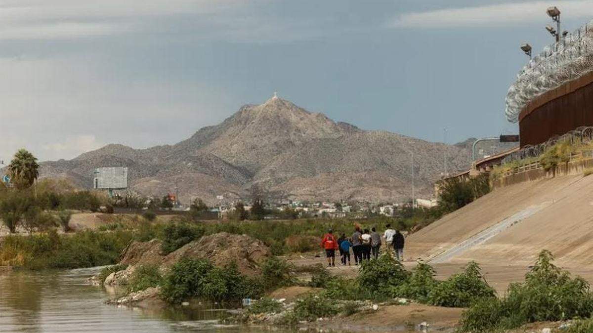 Un grupo de migrantes de Venezuela camina entre el muro fronterizo sur y el Río Grande hacia una instalación temporal de procesamiento de la Patrulla Fronteriza el 6 de octubre de 2022 en El Paso. Crédito: Jordan Vonderhaar para The Texas Tribune