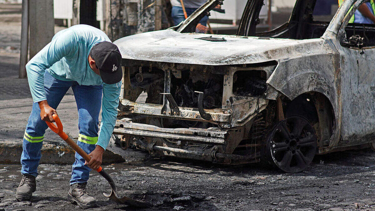Un trabajador limpia una calle en donde hay un automóvil quemado en Puerto Vallarta, estado de Jalisco, México, el lunes 23 de febrero de 2026.